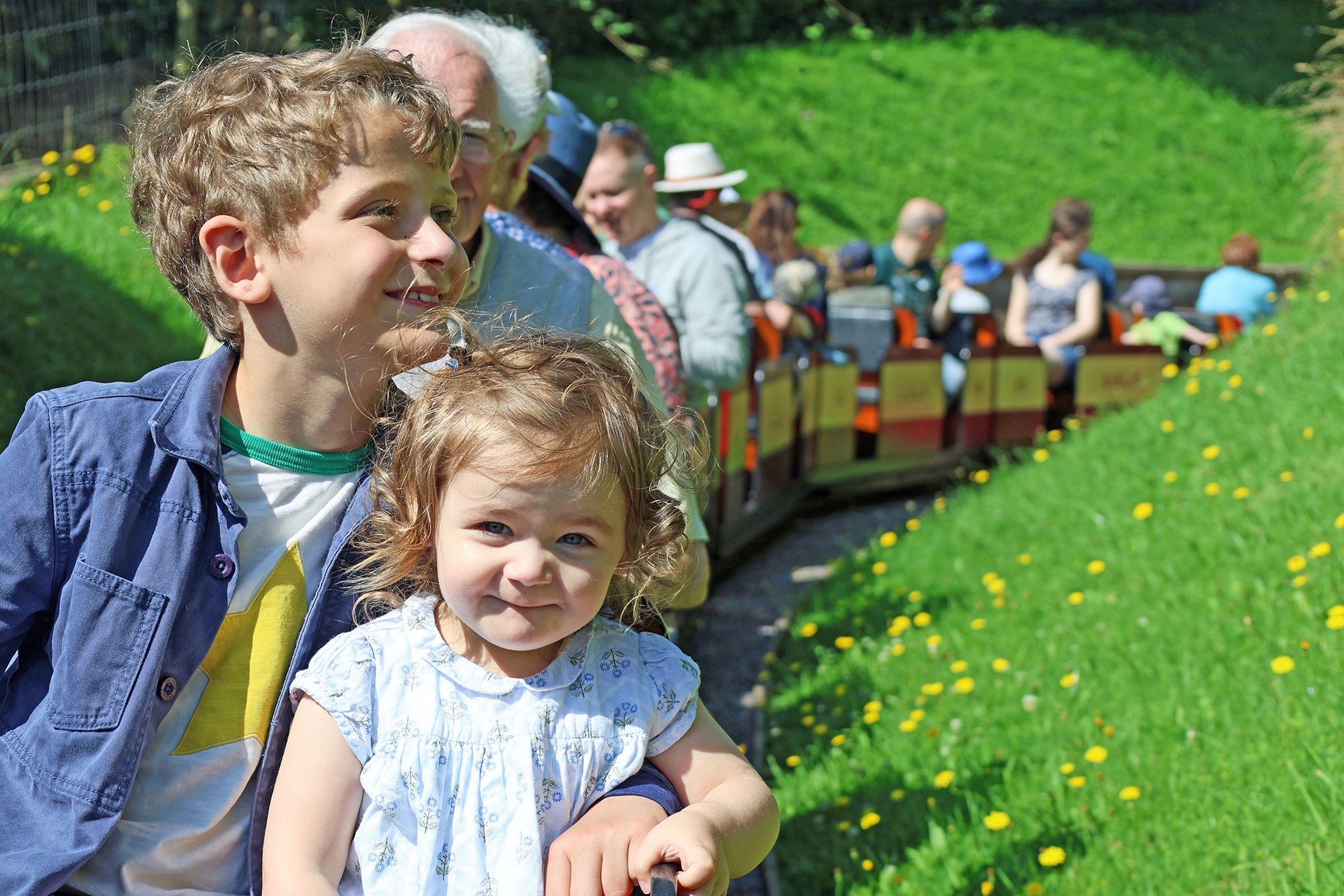 Children sitting on a grassy hill with a miniature train in the background